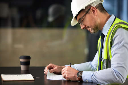 Filling out some paperwork. Cropped shot of a handsome mature male construction worker filling out...