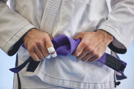 Hes a seasoned professional. Cropped shot of an unrecognizable man tying a purple belt around hist waist while in full jiu jitsu gi.の写真素材