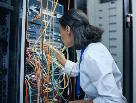 She knows exactly where each cable should be. Cropped shot of an attractive young female programmer working in a server room.の写真素材