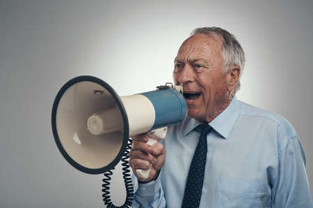Oi Just hear me out. Shot of a senior businessman standing alone against a grey background in the studio and using a megaphone.の写真素材