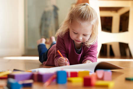 Ill show you my picture when Im done. Shot of a little girl lying on the floor with her colouring...