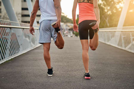 Getting their legs ready for a run. Rearview shot of a young couple warming up on a bridge before...
