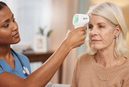 Lets start your physical but first a fever check. Shot of a doctor examining a mature woman with a...