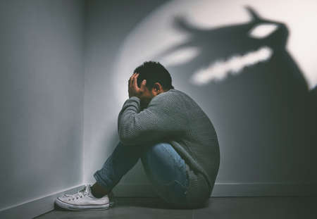 If dreams come true, can nightmares too. Shot of a young man sitting in the corner of a dark room...