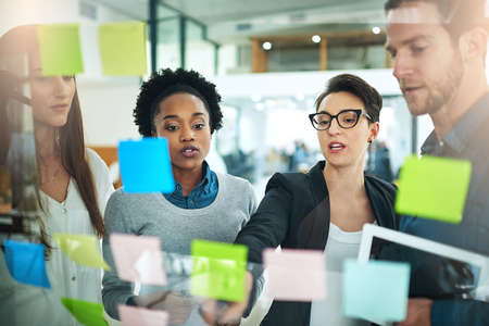 This is our best strategy for success. Cropped shot of coworkers using sticky notes on a glass wall...