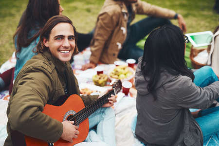 Time to play some tunes. Portrait of a cheerful young man about to play guitar at a picnic with his friends outside during the day.の写真素材