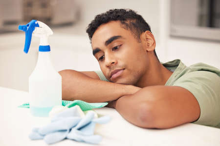 Stuck in a loop of endless cleaning. Shot of a young man looking bored while cleaning his kitchen.の写真素材