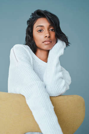 Learn to put yourself first. Shot of a beautiful young woman sitting on a chair against a teal...
