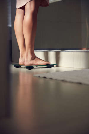Stop weighing yourself down. Shot of an unrecognizble woman weighing herself on a scale at home.の写真素材