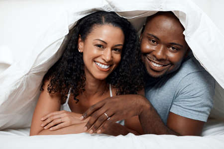 Always in a good mood together. Portrait of a cheerful young couple lying in bed together under a...