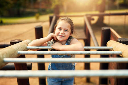 The park is her favourite place to enjoy endless fun. Portrait of a little girl playing on the jungle gym at the park.の写真素材