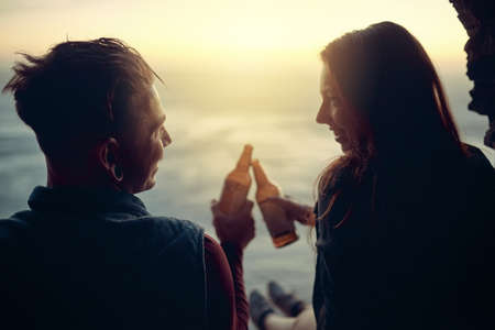 To a well deserved drink. Cropped shot of an affectionate young couple toasting with beers atop a...