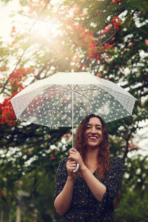 Some people look at rain and frown, not her. Cropped shot of a beautiful young woman walking in the rain outside.の写真素材