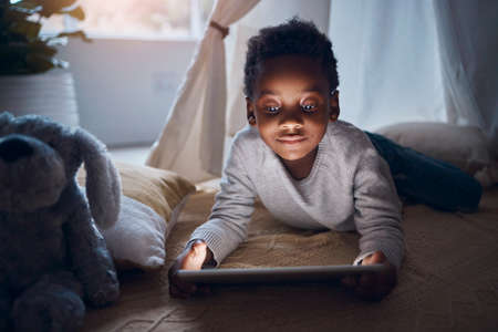 I have so many stories. Shot of a little boy using his digital tablet while lying on the floor.の写真素材