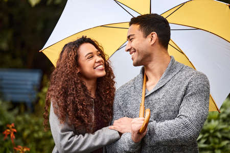 We can get through the storm together. Shot of a young couple standing in the rain with an umbrella.の写真素材