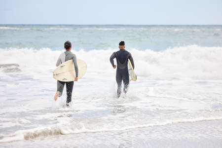 We belong in the ocean. Shot of an unrecognizable couple running into the water with surfboards at...