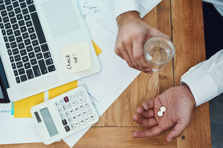 Taking some painkillers to knockout a headache. High angle shot of an unrecognisable businessman...