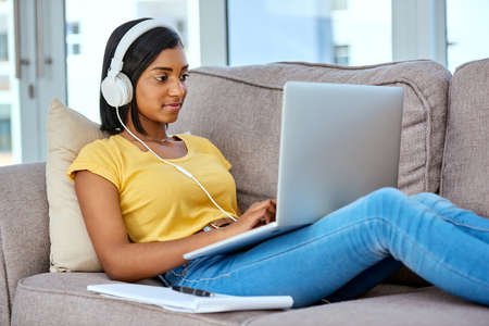 Downloading all my favourite tracks. Shot of a teenage girl listening to music and using a laptop at...
