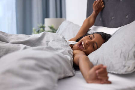 Youre a good nights rest away from a good mood. Shot of a young woman yawning and stretching while...