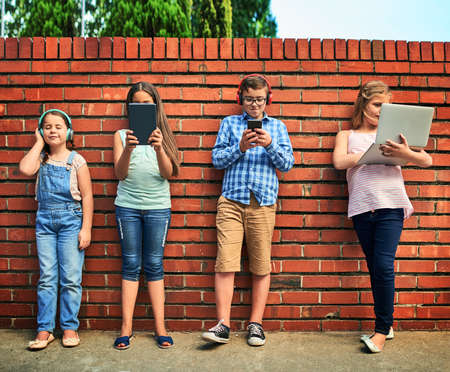 Childhood in the digital age. Shot of a group of young children using digital devices against a...