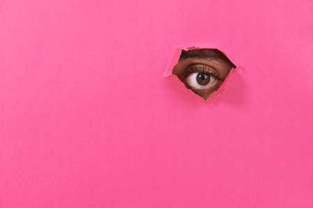I see you. A view of a mans eye looking through a hole in some colorful paper.の写真素材