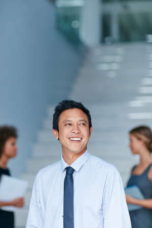 It feels amazing to inspire others. Cropped shot of a young businessman standing in an office with colleagues in the background.の写真素材