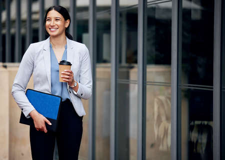 Productivity lies in the bottom of this cup. Shot of a young businesswoman enjoying a cup of coffee while making her way work.の写真素材