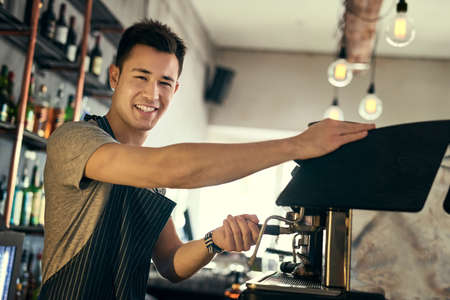 What can I get you. Cropped portrait of a young barista preparing drinks in his coffee shop.の写真素材