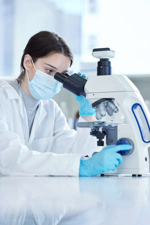 It looks a lot different under the lens. Shot of a young woman using a microscope in a lab.の写真素材