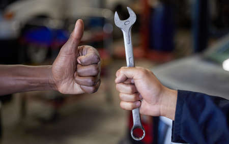 Thumbs up for maintenance. Closeup shot of one mechanic holding a spanner and another giving thumbs up in their workshop.の写真素材