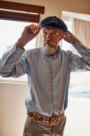 Hes a stylish senior. Portrait of a cheerful senior man trying on one of his hats while looking at the camera.の写真素材