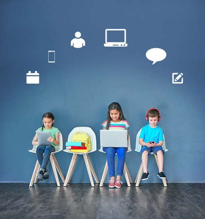 Todays child is more connected than ever before. Studio shot of kids sitting on chairs and using wireless technology with technological icons above them against a blue background.の写真素材