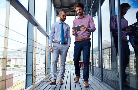 Performing at their optimum through effective teamwork. Shot of two young businessmen using a digital tablet together outside of an office building.の写真素材