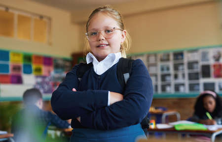 Education is the focus. Shot of a young girl standing in her classroom at school with her arms folded.の写真素材