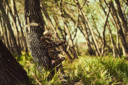 Hes a great little marksman. Shot of a cute little boy in camouflage playing with his bow and arrow in the woods.の写真素材