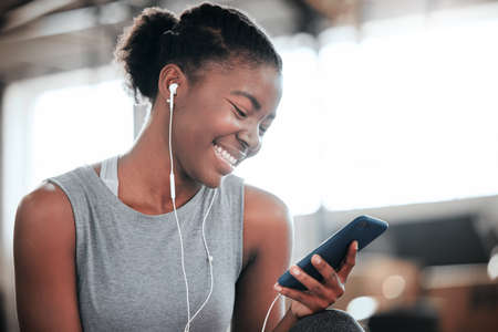 You can almost hear her smile. Shot of a young beautiful woman using her cellphone and earphones at...