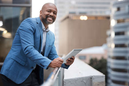 Its how I stay ahead. Portrait of a mature businessman using a digital tablet while standing on a balcony outside an office.の写真素材