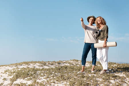 What about there. Full length shot of two attractive mature woman standing with their on the beach.の写真素材