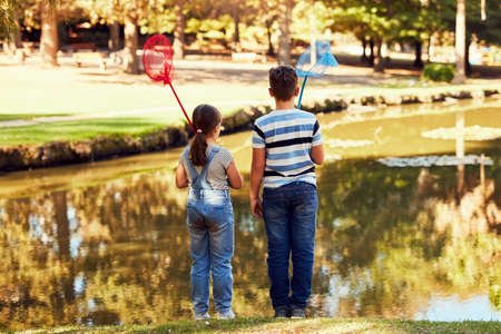 Here fishy fishy.... Rear view shot of two young siblings holding fishing nets at a lake in the park.の写真素材