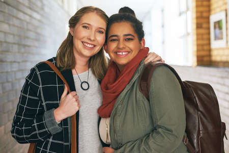 Campus is better with her by my side. Portrait of two attractive young female university students standing in a campus corridor.の写真素材