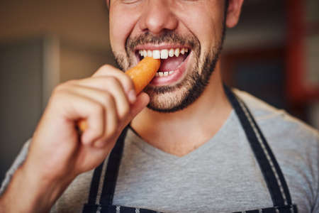 Hes got a carotene craving. Cropped shot of an unidentifiable young man eating a carrot in his...