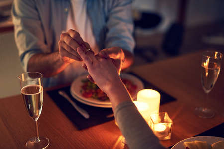 The perfect occasion. Cropped shot of an unrecognizable man proposing to his wife over a candle lit dinner at night.の写真素材