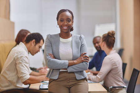 With this team behind me, its easy to be confident. Cropped portrait of an attractive young businesswoman standing with her arms folded in the boardroom with her colleagues in the background.の写真素材