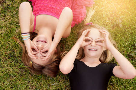 What fun it is to be kids. Portrait of two little girls having fun while lying on the grass outside.の写真素材