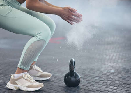 Hard muscles coming right up. Shot of an unrecognisable woman dusting her hands with chalk powder before working out with kettle bell weights in a gym.の写真素材