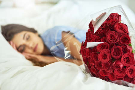 Shes got a surprise waiting for her. Cropped shot of an attractive young woman asleep beside a bouquet of roses in her bed.の写真素材