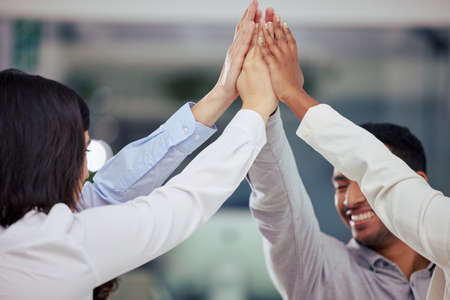High five for a good days work. Shot of a group of businesspeople giving each other a high five at...