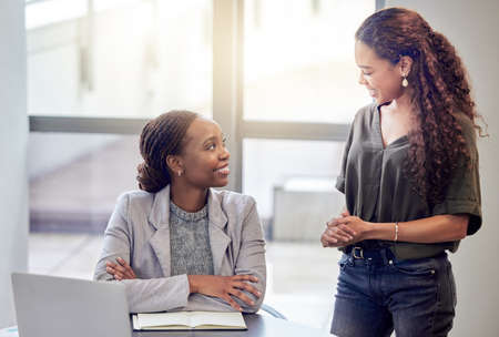 Do you need any help. Shot of two young female colleagues talking while using a laptop in an office at work.の写真素材