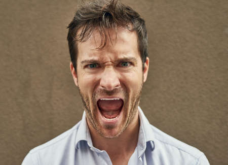 Hes about to bite someones head off. Portrait of an angry young man standing against a dark...