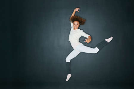 Studio shot of an attractive young woman dancing against a gray background.